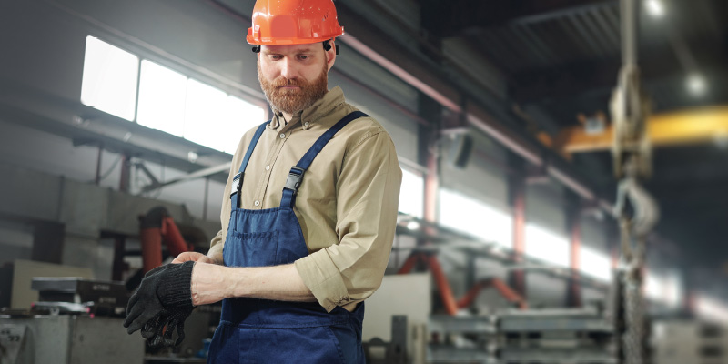A man wearing worker close and a construction hat is putting on a set of worker gloves