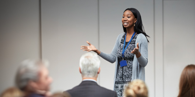 A woman speaks to a crowd of people at a conference