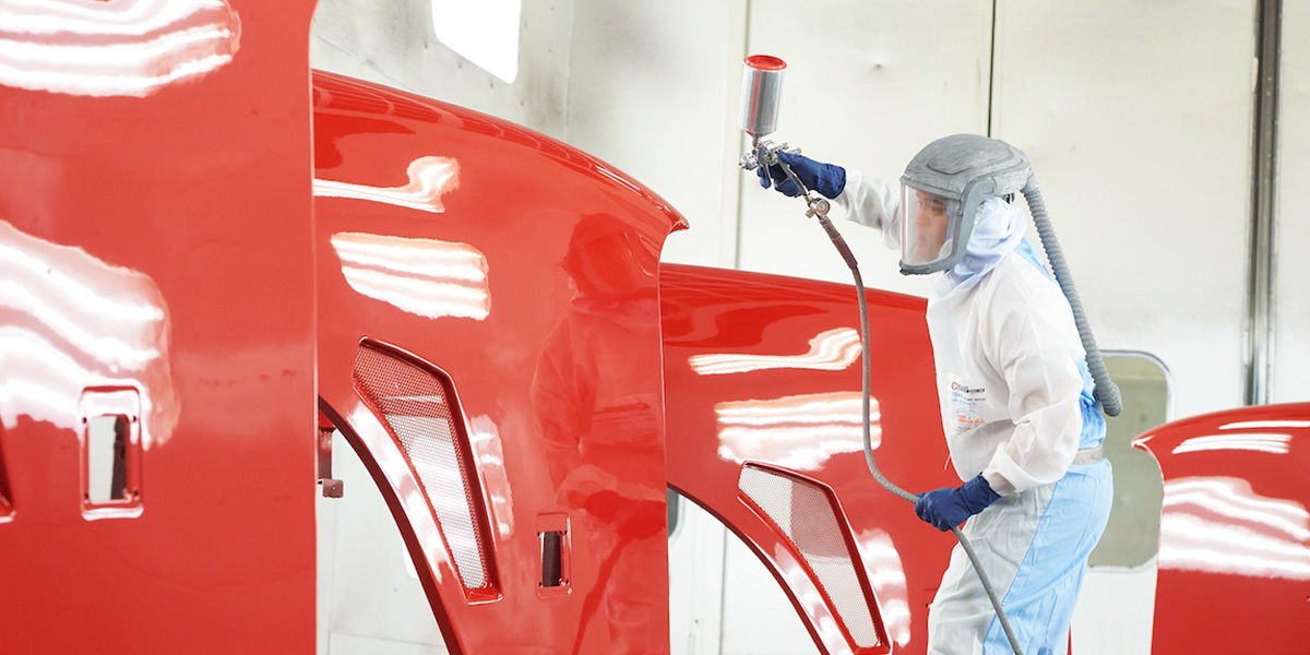 An Eastside Group employee in a sealed working suit applying a coating using a spray gun to vehicle body parts